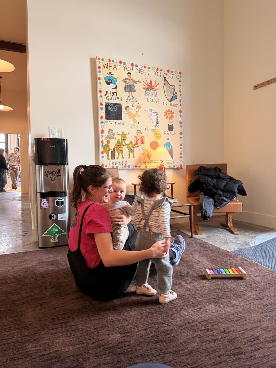 A Rising Stars teacher with two young children in the lobby, the hand-painted music mural on the wall behind them